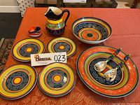 Photo of the entire lot showing the handmade Spanish pitcher, small dish, Pier 1 large pasta bowl, salad bowl, four matching plates, and salad utensils arranged on the table.