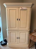 Front view of large ivory cream Lane armoire hutch, showing two pairs of paneled doors with black metal handles, closed.