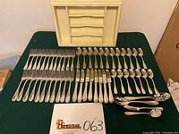 Full flatware set laid out on green cloth with included wooden storage box positioned behind.