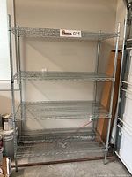 Front view of the stainless steel shelving unit showing four wire mesh shelves with metal frame support.