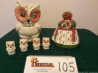 Group shot of the Carol Gifford cookie jar, Shawnee Pottery owl cookie jar, and four owl salt and pepper shakers on green cloth