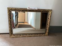 Full view of the vintage wall mirror showing the ornate carved frame with gold and black paint, clear reflective glass, and rectangular shape.