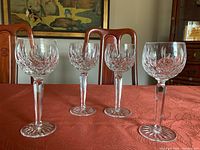 Four Lismore crystal goblets arranged in line on red tablecloth, dining chairs and painting in background