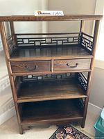 Front view of wooden display shelf showing two drawers with metal handles and fretwork side panels.