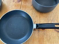 Image of one small frying pan featuring black non-stick interior and black handle on wooden surface