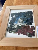 Photo of a wooden framed artwork featuring a cutout style image of The White House with pixelated edges, showing trees and pink flowers around the building.