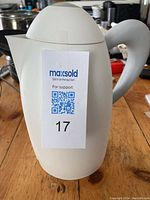 White hot/cold carafe with lid and handle placed on wooden table, photo shows front side with handle and lid visible.