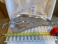 Full view of shiny metal serving plate shaped like a hot pepper, placed on a white towel with a measuring tape showing length about 16 inches.