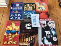 Image showing six paperback books arranged on a wooden surface. Titles include Moon Music and Straight Into Darkness by Faye Kellerman, Night Fall by Nelson DeMille, Charley's Web by Joy Fielding, The Book Thief by Markus Zusak, and 21: Bringing Down the House by Ben Mezrich.