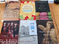 Top view of six paperback books arranged in two rows of three on a wooden surface. Titles are visible showing author names and covers.