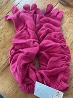 Pair of bright pink gloves laid flat on wooden surface, showing ruched fabric detail and overall shape.