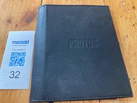 Front exterior view of black leather photo binder with 'PHOTOS' embossed on the cover.