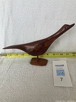 Photo from side showing the full length and shape of the wooden bird figure with measuring tape indicating length.