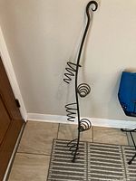 Full view of black wrought iron wine bottle holder with five bottle holders and decorative curled iron at top and bottom.