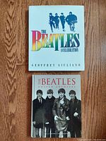 Top view of two Beatles hardcover books, "A Celebration" and "Unseen Archives", placed on a wooden surface.