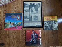 Overview of all four items in the lot on a wooden floor: framed Rolling Stones album art page, David Bowie biography book, Punk history book, and The Album Cover Album book.