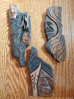 Top view of the three carved bark warrior faces placed on wood floor, showing varying sizes and detailed facial carvings with natural bark bases.