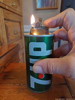 Lighter held in hand while lit, showing the flame and ignition mechanism on top of the soda can shaped lighter.