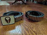 Two black leather bullet belts coiled, showing bullet details and buckles on wood floor.