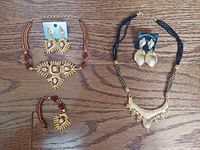 Five sets of gold-tone fashion jewelry including necklaces, earrings, and bracelets displayed on wooden surface. Detailed, colorful gem embellishments visible.