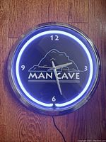 Front view of the round quartz clock with white fluorescent light and 'MAN CAVE' design on the black face with chrome rim.