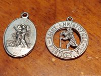 Two sterling silver Christian saint medallions side by side, one oval with an angel and child, one circular with Saint Christopher inscription