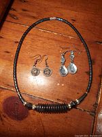 Photo of the hematite bead necklace and two pairs of dangle earrings on wooden surface.