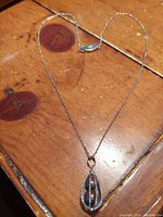 Full view of silver chain necklace with amber pearl teardrop pendant on wooden surface.