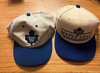 Front view of two Toronto Maple Leafs baseball style hats, showing logos and brim color.