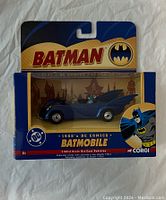 Front view of sealed 1960s blue Batmobile die-cast car model in blister packaging with Batman themed graphics and Corgi branding.