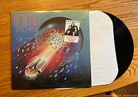 Front cover of Journey Escape vinyl record album with vinyl partially pulled out of white inner sleeve, showing colorful artwork of a scarab beetle rocket breaking through glass and album title at top left.