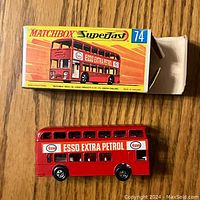 Red painted double-decker bus toy with 'Esso Extra Petrol' decals and black and silver wheels shown with the original Matchbox Superfast yellow and orange box, with box partially open.