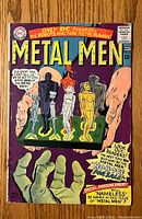Front cover of Metal Men #16 comic book showing the team characters on a green platform held by a giant hand, with bold colorful text and pricing.