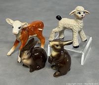 Overview photo showing all four figurines together on a flat grey surface with the lamb elevated on a clear display riser.