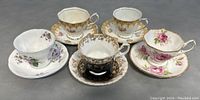 Top down photo of all five teacup and saucer sets showing floral designs and gold trim.
