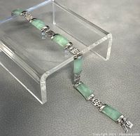 Photo of the full length of the sterling silver bracelet with green stone links laid on display stand.