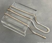 Silver necklace and bracelet displayed on a clear stand showing the chain links and clasps.