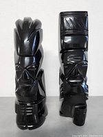 Front view of two black obsidian hand carved Aztec and Mayan stone sculptures showing detailed facial and geometric features.