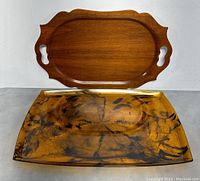 Two trays: one rectangular faux tortoise shell lucite tray in amber and black pattern, and one wooden tray with scalloped edges and handles.