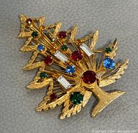 Front angle view of the gold-tone Christmas tree brooch with various colored stones.