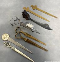 Full set of 9 vintage collectible letter openers and silver plated candle snuffer laid out on neutral background