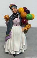 Front view of vintage Royal Doulton Biddy Penny Farthing figurine, woman with colorful balloons and flowers, showcasing detailed clothing and facial features.