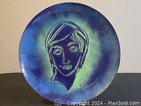 Full view of the round brass plate showing the entire hand painted portrait of a woman with blue and green hues.