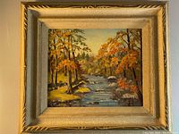 Framed oil painting showing the full piece including decorative gold-colored frame, with autumn scenery and flowing river.