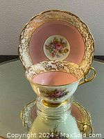 Teacup and saucer standing vertically showing the pink interior, gold trim, and detailed floral design on cup and saucer.