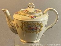 Side view of the teapot showing floral decorations, gold details, curved handle, and repaired spout.