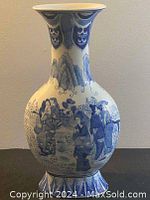 Front view of oriental blue and white vase featuring traditional figures and mountain motifs with flared rim.