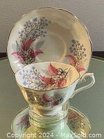 Porcelain teacup and saucer with pink and purple floral design, displayed on a reflective glass surface.