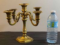 Front view of the solid brass 4-arm candelabra next to a standard water bottle for size reference.