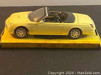 Side angle of yellow Thunderbird die cast model car on yellow base showing clear windshield, detailed wheels, and convertible interior.